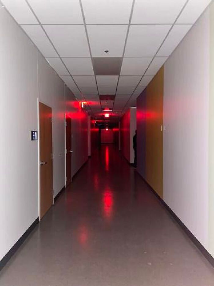 A long, eerie liminal space in a hallway with red emergency lights creating an ominous glow.