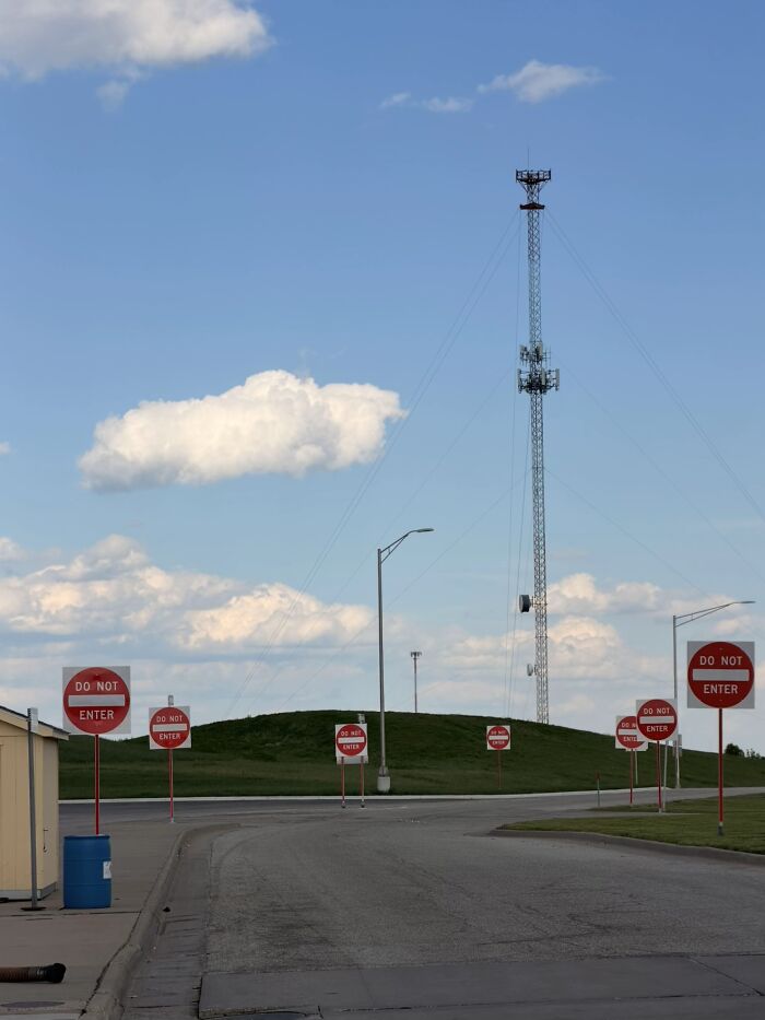 Numerous DO NOT ENTER signs block a road leading to a hill with a tall antenna, a haunting liminal space.