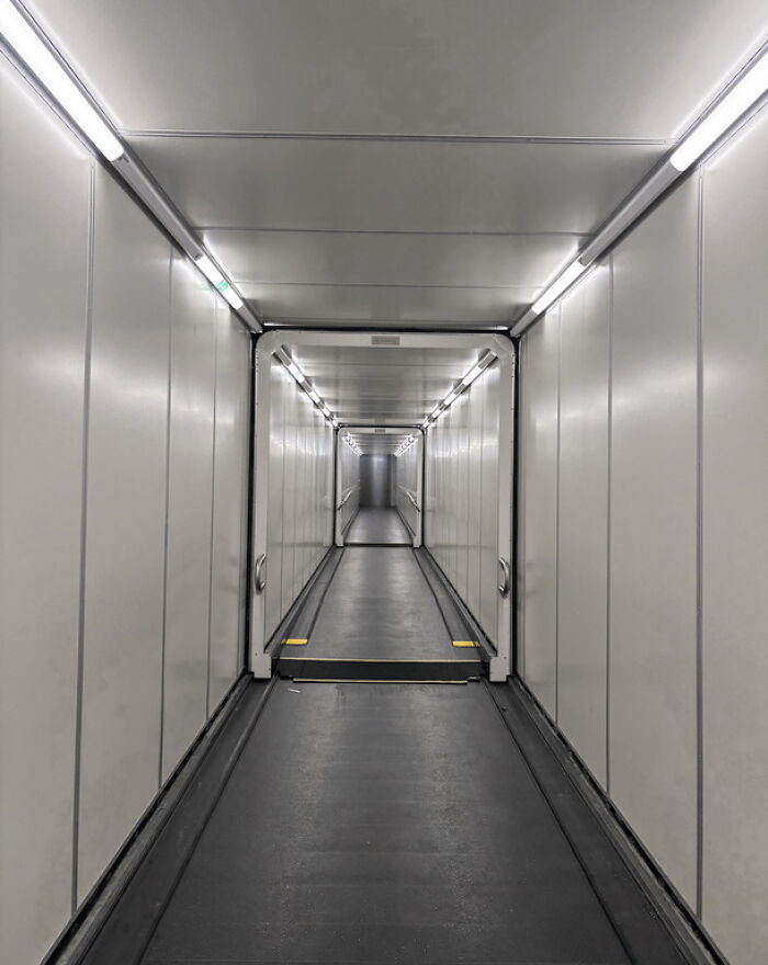 A long, empty jet bridge walkway creates an unsettling liminal space. The sterile environment descends into the abyss.