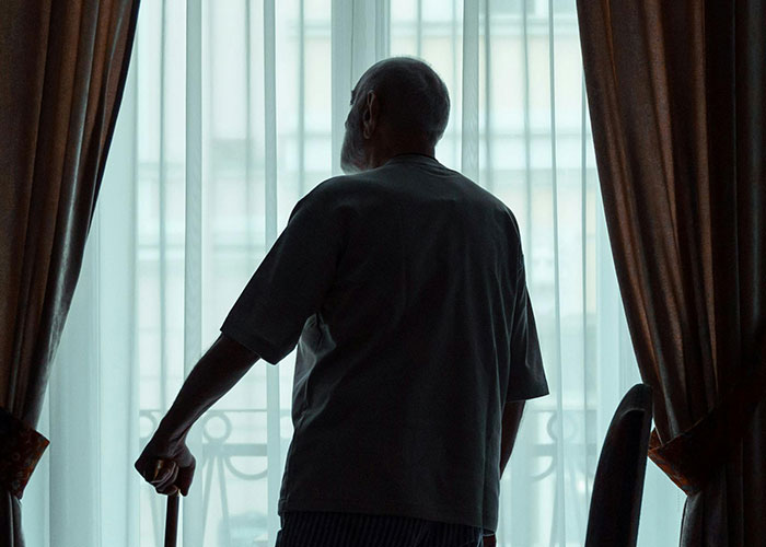 Elderly man standing by window with cane
