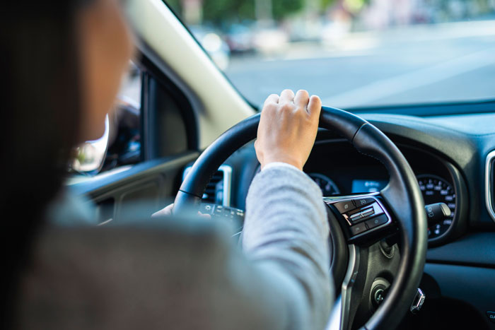 Person driving car holding steering wheel focused on road