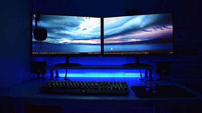 Dual computer monitors with illuminated keyboard in dark gaming setup