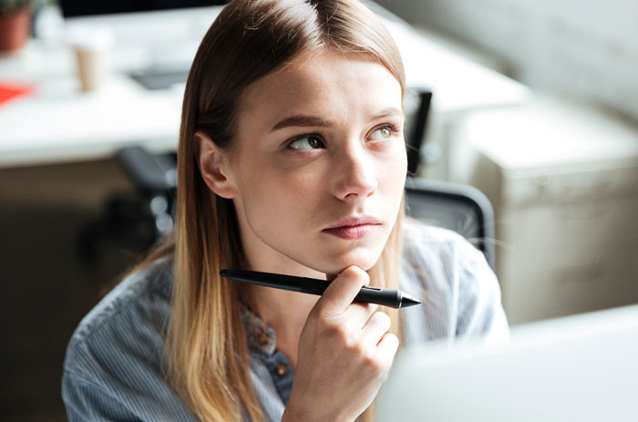 Woman looking thoughtfully holding pen in office setting about body comments
