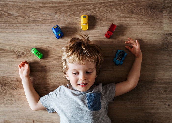 A young boy lying on the floor surrounded by toy cars, representing various conditions and brain triggers like autism. A young boy lying on the floor surrounded by toy cars, representing various conditions and brain triggers like autism.