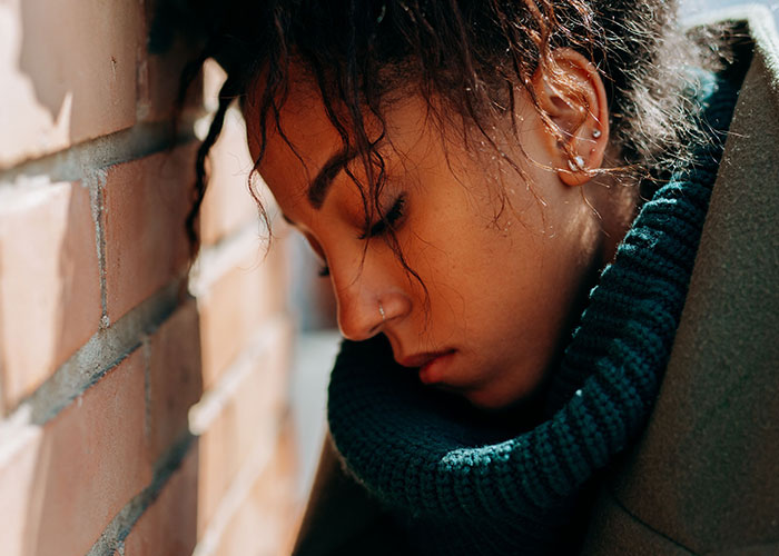 A woman leans against a brick wall, eyes closed, reflecting on things committed by close friends that broke people's trust.