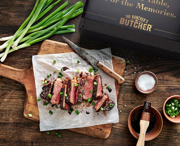 Sliced grilled steak on wooden board with green onions and seasoning