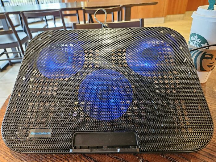 A laptop cooling pad with glowing blue fans on a wooden table, part of Prime Day Electronics Deals.