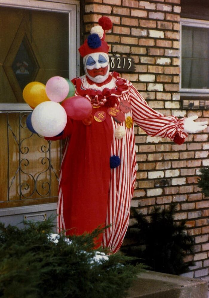 Serial killer dressed as clown holding balloons outside brick house