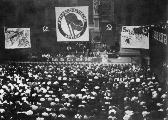 Historical photos: A large crowd gathered in a hall with banners of political groups.