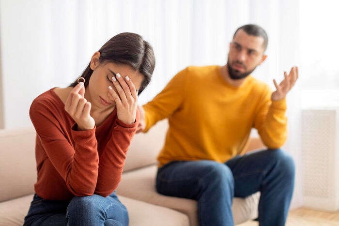 Woman holding ring stressed as man argues, unhappy couple breakup excuses