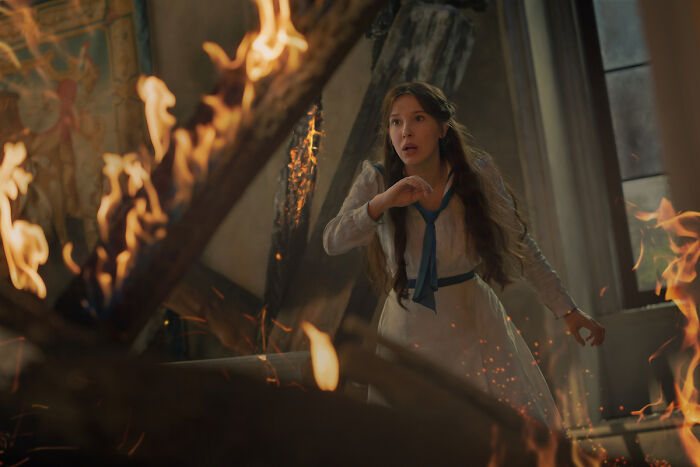 Millie Bobby Brown looks startled, surrounded by flames and debris in an intense scene from Enola Holmes 3. Millie Bobby Brown looks startled, surrounded by flames and debris in an intense scene from Enola Holmes 3.