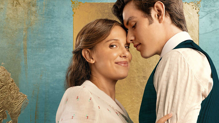 Millie Bobby Brown smiles at the camera, leaning against Louis Partridge in a promotional image for Enola Holmes 3. Millie Bobby Brown smiles at the camera, leaning against Louis Partridge in a promotional image for Enola Holmes 3.