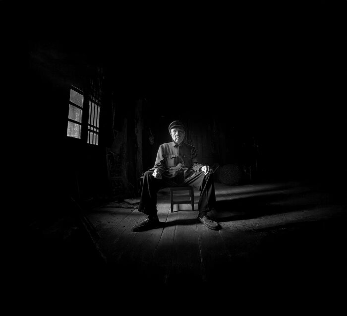 Dramatic black and white portrait of elderly man seated in dark room capturing raw human spirit
