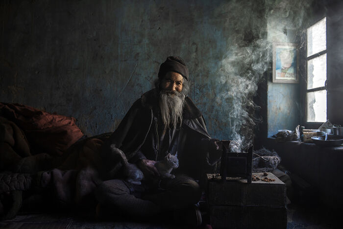 Portrait of elderly man with beard beside smoky fire depicting raw beauty of spirit