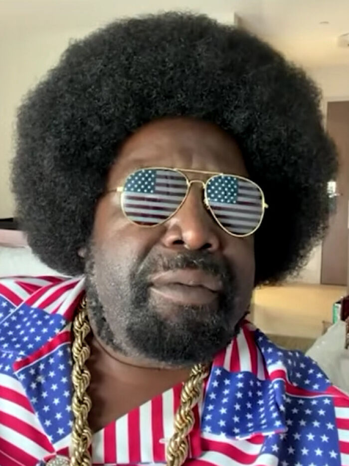 A man with a large afro and USA flag sunglasses, showcasing celebrity scandals.