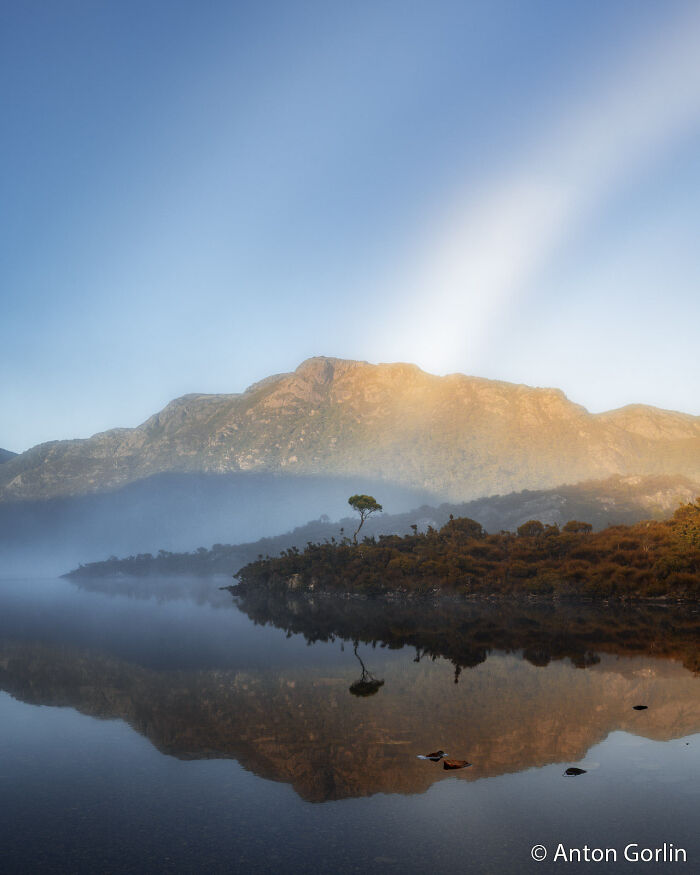 Serene lake reflecting a mountain and a single tree under a clear sky, part of the Au Photo Contest.