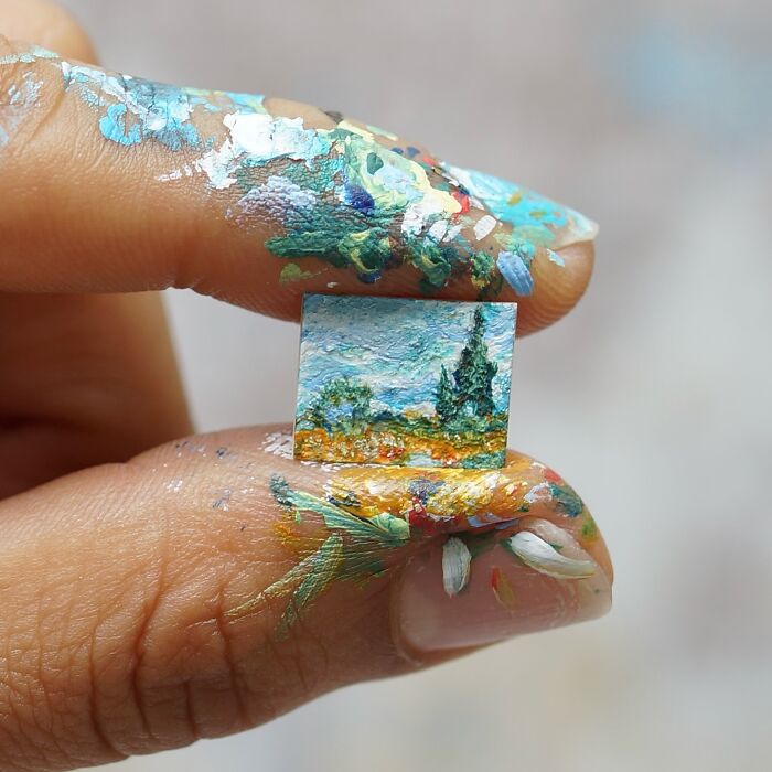 Miniature paper figures: A detailed landscape painting barely held by paint-stained fingers, highlighting immense detail.