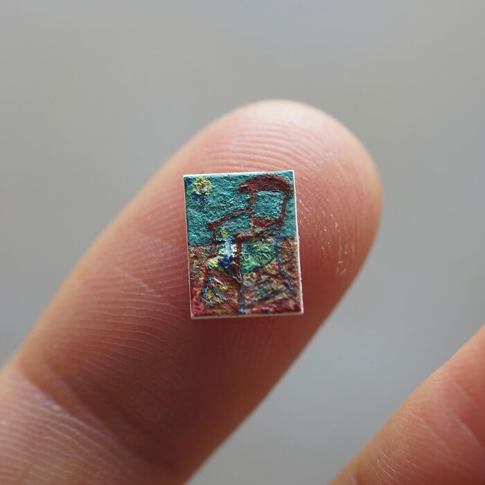 A highly detailed miniature paper figures painting, resembling a landscape with vibrant colors, held between two fingers.