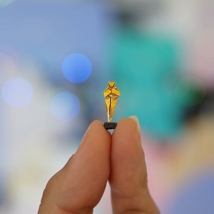 A tiny, golden origami figure held between two fingers, showcasing immense detail in miniature paper figures.