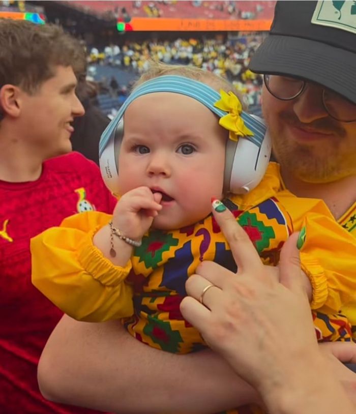 Baby with ear muffs at World Cup in yellow outfit being held by parents; an alert was sent by doctors.