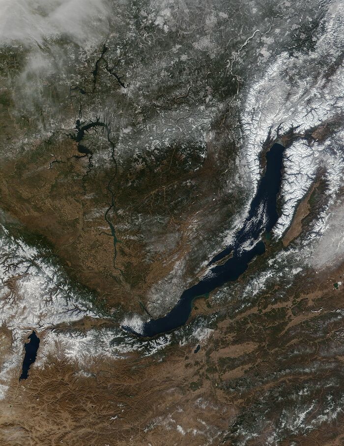 Satellite image of Lake Baikal surrounded by snowy mountains and land, showcasing interesting facts about Earth.