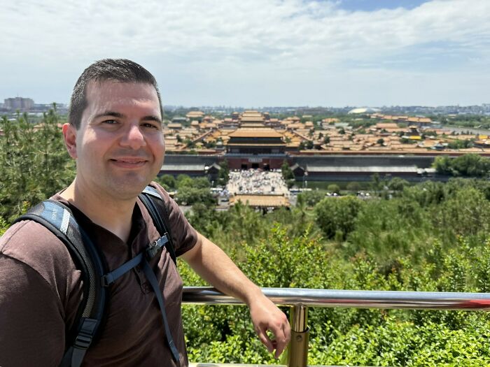 Traveler smiles, with the vast, historic Forbidden City in China visible in the background, a unique travel destination.