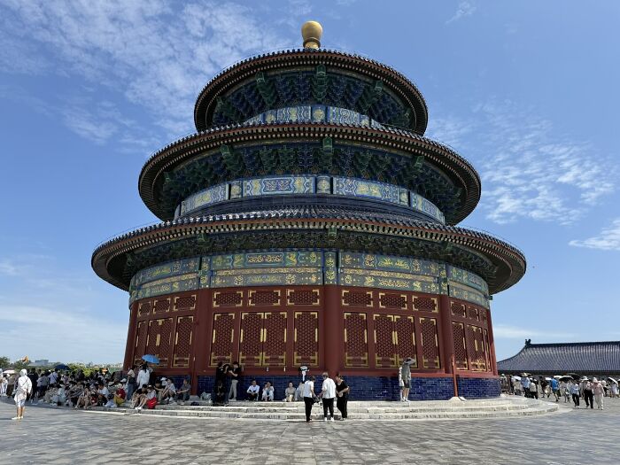 Traveler in China, visiting a magnificent multi-tiered temple with intricate blue and gold details under a clear sky.