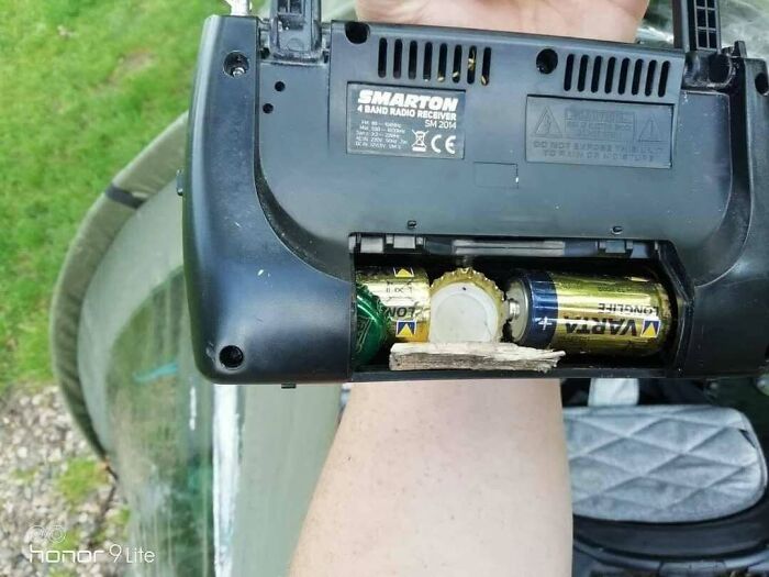 A hand holding a radio with bottle caps and cardboard used as batteries, an example of Slavic Science.