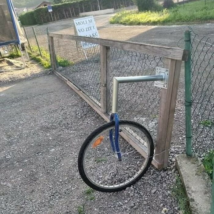 A fence post with a bicycle wheel and fork as a makeshift gate latch, showcasing Slavic Science ingenuity.