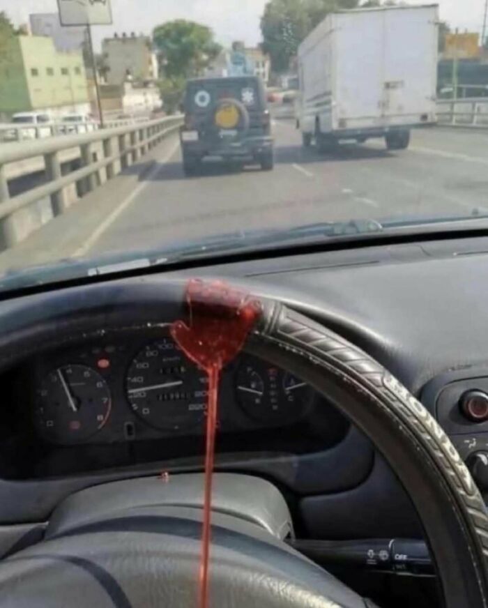 Blood-like substance on car steering wheel with view of road and vehicles ahead