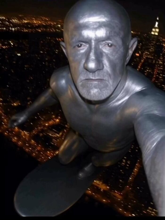 Man painted silver posing as statue surfing above city at night