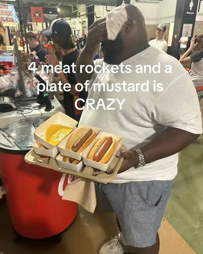 Man holding tray with four hot dogs and mustard plate showing random sense of humor