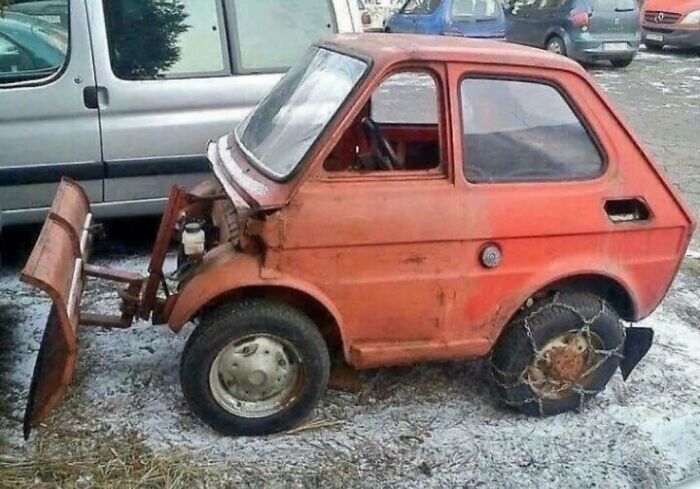 Rusty tiny car modified with a plow and snow chains on tires