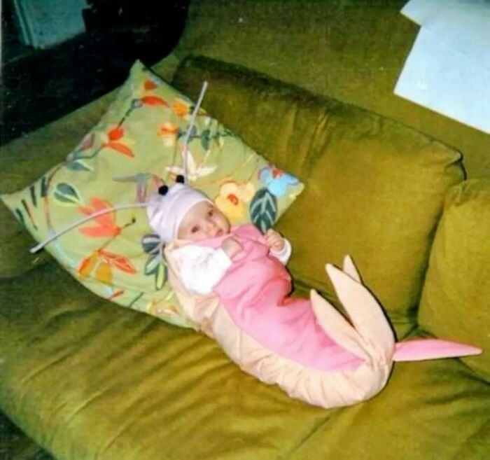 Baby dressed in pink sea creature costume lying on green couch pillow