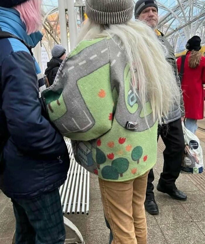 Person wearing a jacket with a road and landscape pattern at a crowded public space