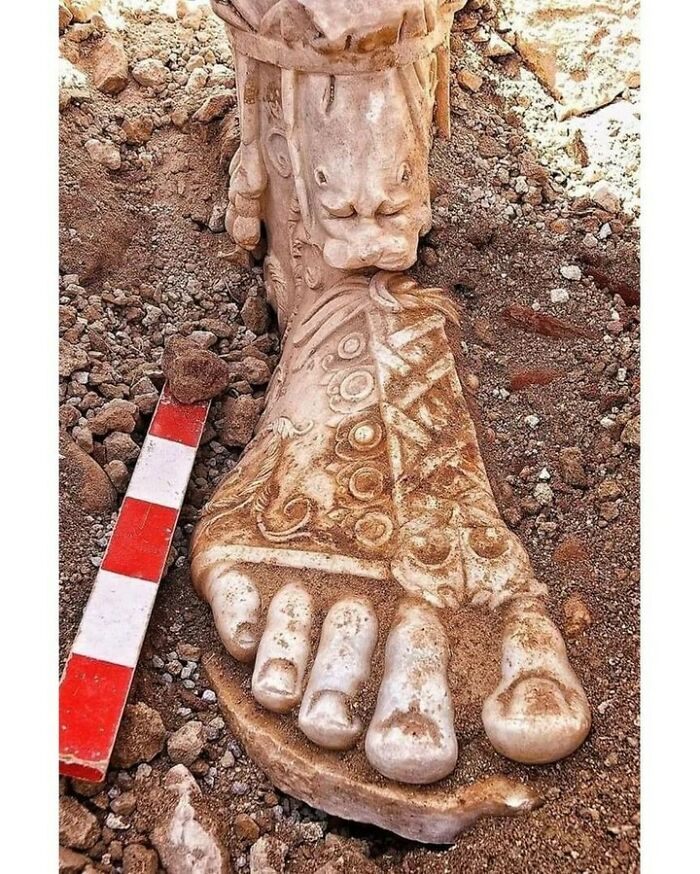 Ancient historical treasure of ornate stone foot sculpture partially unearthed in dirt
