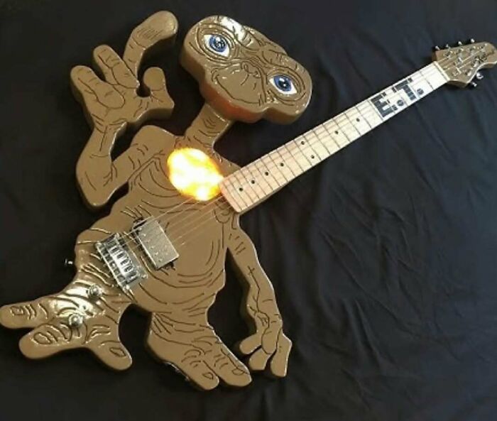 Guitar shaped like E.T. alien figure with glowing heart detail on black background