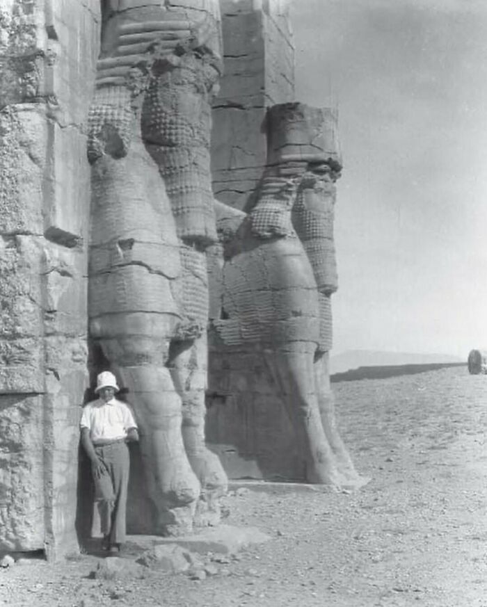 Black and white photo of giant Assyrian statue with person standing beside historic ruins