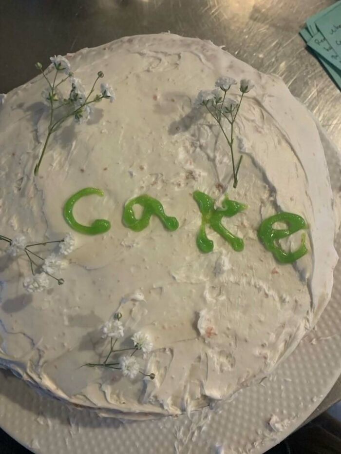 Cake with uneven white icing and green writing spelling cake