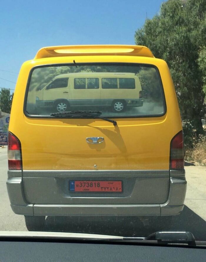 Yellow and gray van with rear window showing reflection of another similar van