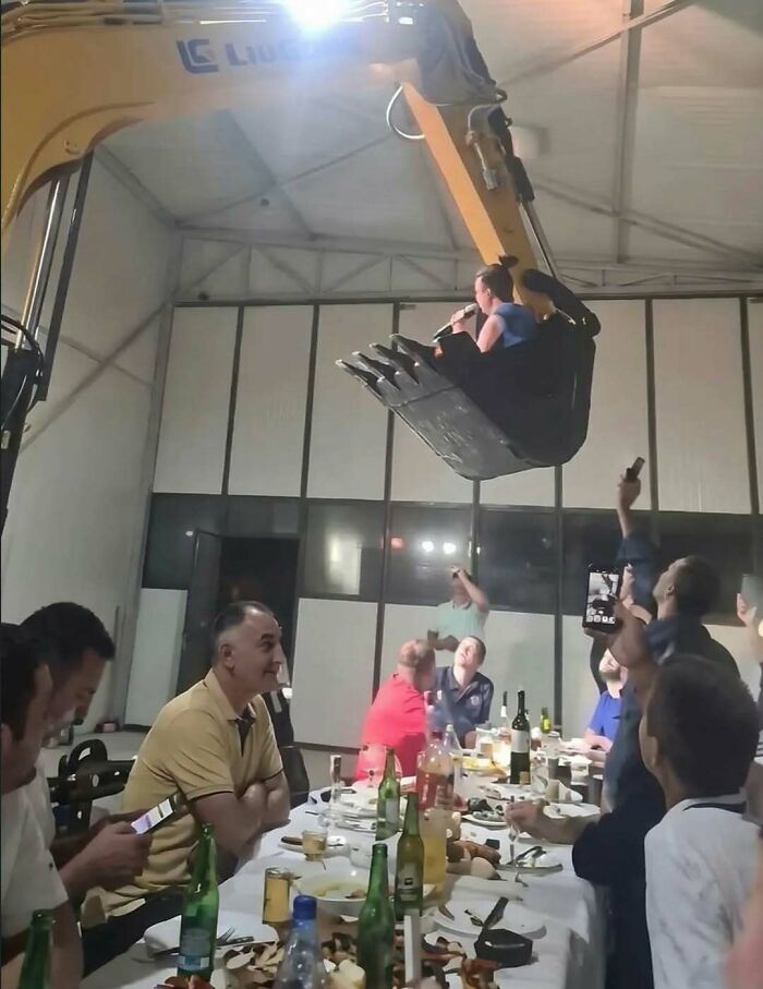 Man singing from excavator bucket as audience watches at party