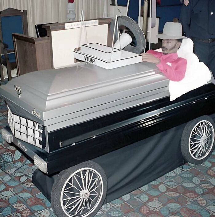 Cursed image of a coffin car with a man lying inside wearing a hat