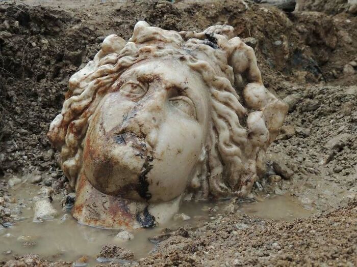 Unearthed ancient sculpture head partially covered with soil and mud