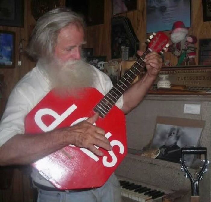 Man playing guitar shaped like stop sign with visible letters in rustic room