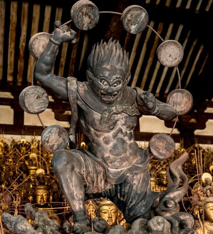 Ancient Japanese bronze statue of a fierce deity surrounded by circular elements inside temple