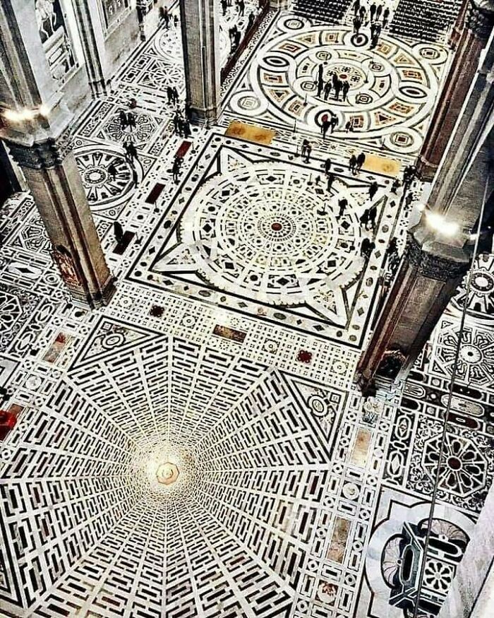 Intricate historical mosaic floor with geometric patterns and visitors walking inside cathedral