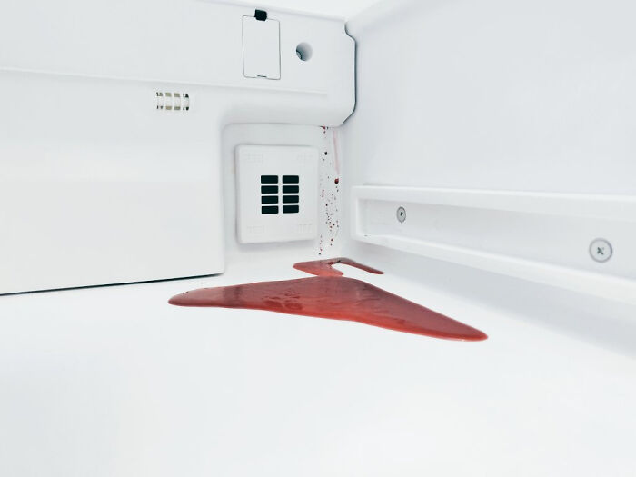 A deeply unsettling liminal spaces image of red liquid spilling and forming a hanger shape inside a white refrigerator.