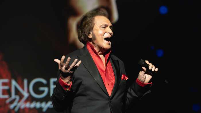 Engelbert Humperdinck, a celebrity whose fame ran out, performing on stage in a black suit and red shirt.