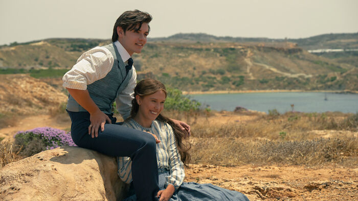Millie Bobby Brown as Enola Holmes and Louis Partridge as Tewkesbury in Enola Holmes 3, overlooking a scenic landscape with water. Millie Bobby Brown as Enola Holmes and Louis Partridge as Tewkesbury in Enola Holmes 3, overlooking a scenic landscape with water.