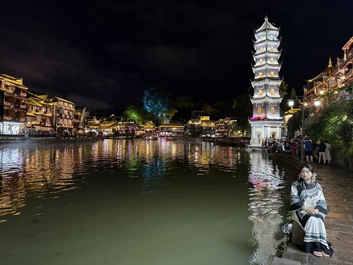 A tranquil night scene in China with traditional illuminated buildings and a pagoda reflecting on the river, inviting travelers.